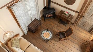 A cozy room with a wooden floor, a sofa, a table with a board game, a chair, a small table with flowers, and a fireplace.