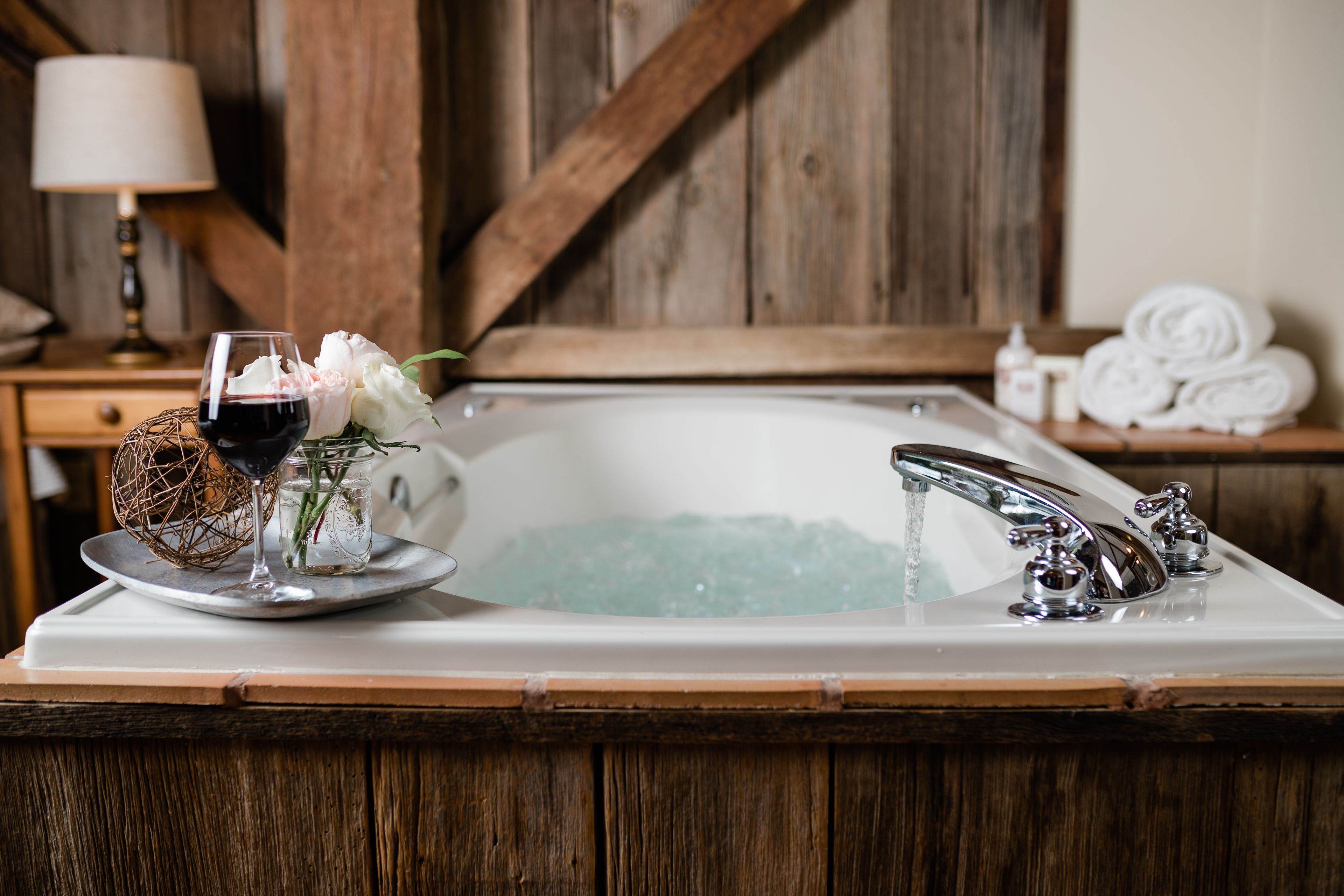 Un baño con bañera, lavamanos y espejo. Hay una botella de loción y toallas a un lado.