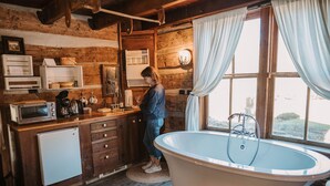 Ein rustikales Blockhaus-Interieur mit Holzausbau, einer großen Badewanne, einer Küchenzeile und einem Fenster mit Vorhängen.