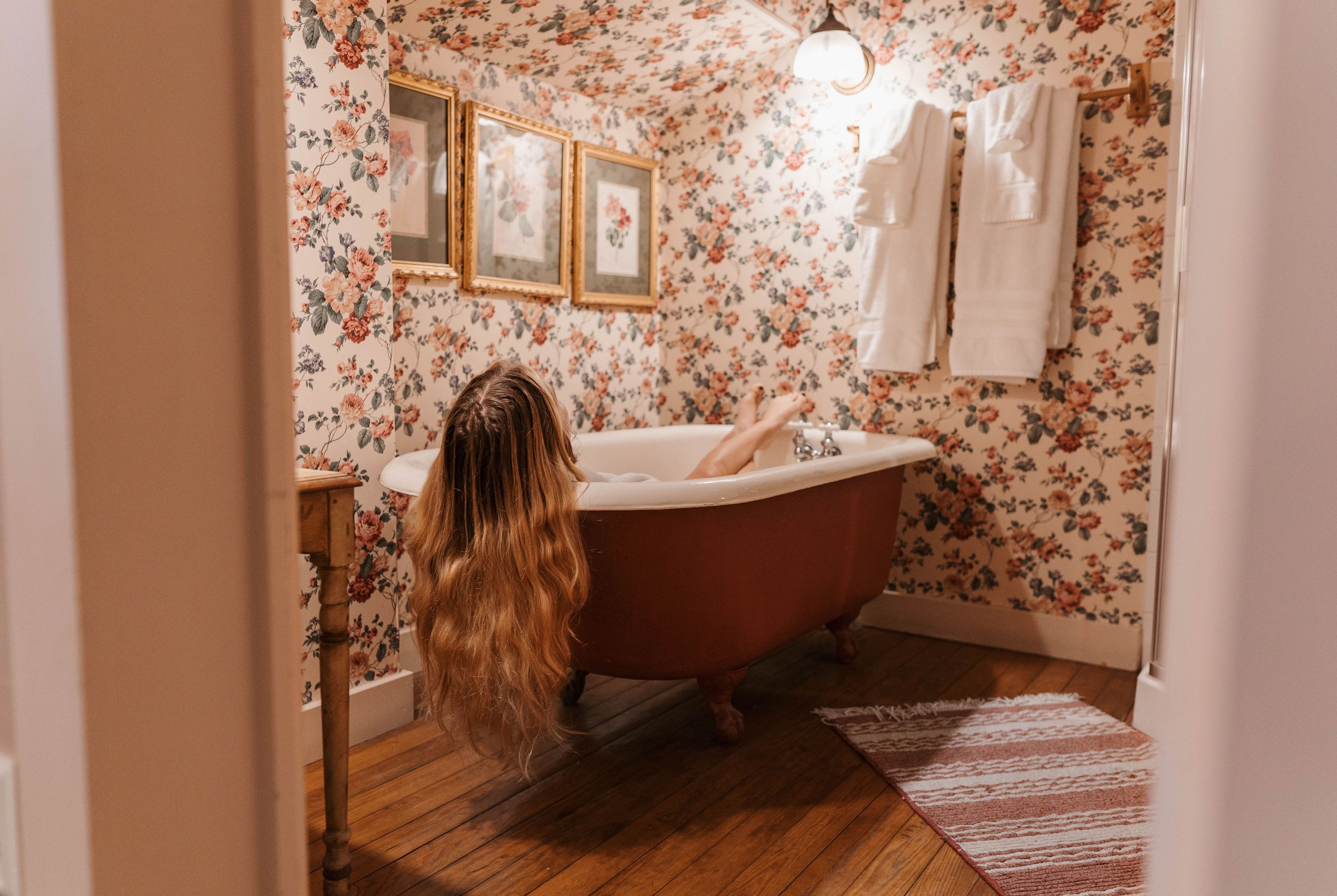 A bathroom with floral wallpaper, a vintage clawfoot bathtub, and a wooden floor.