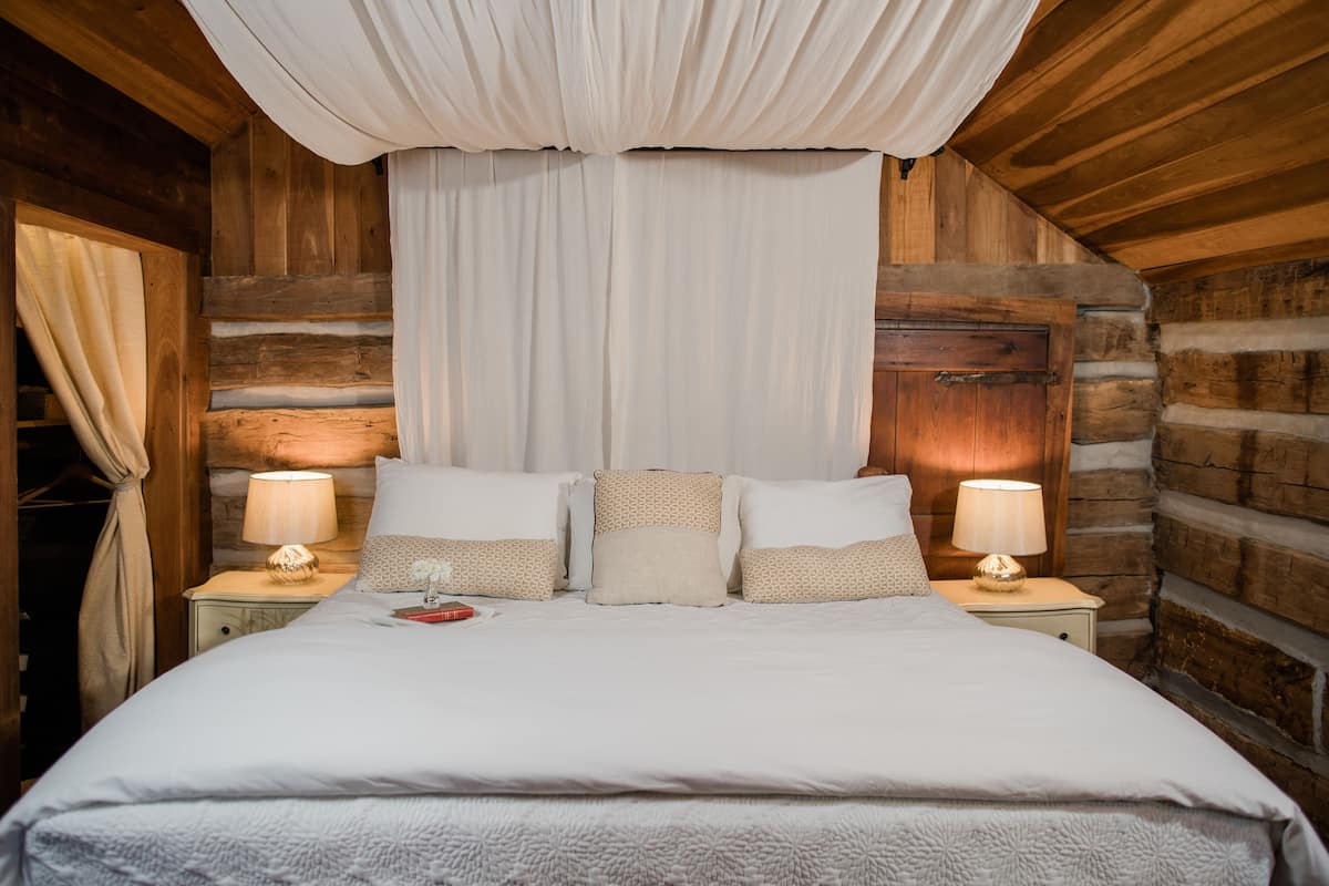 Un dormitorio de cabaña de madera con una cama grande, dos mesitas de noche con lámparas y una cortina sobre la cama.