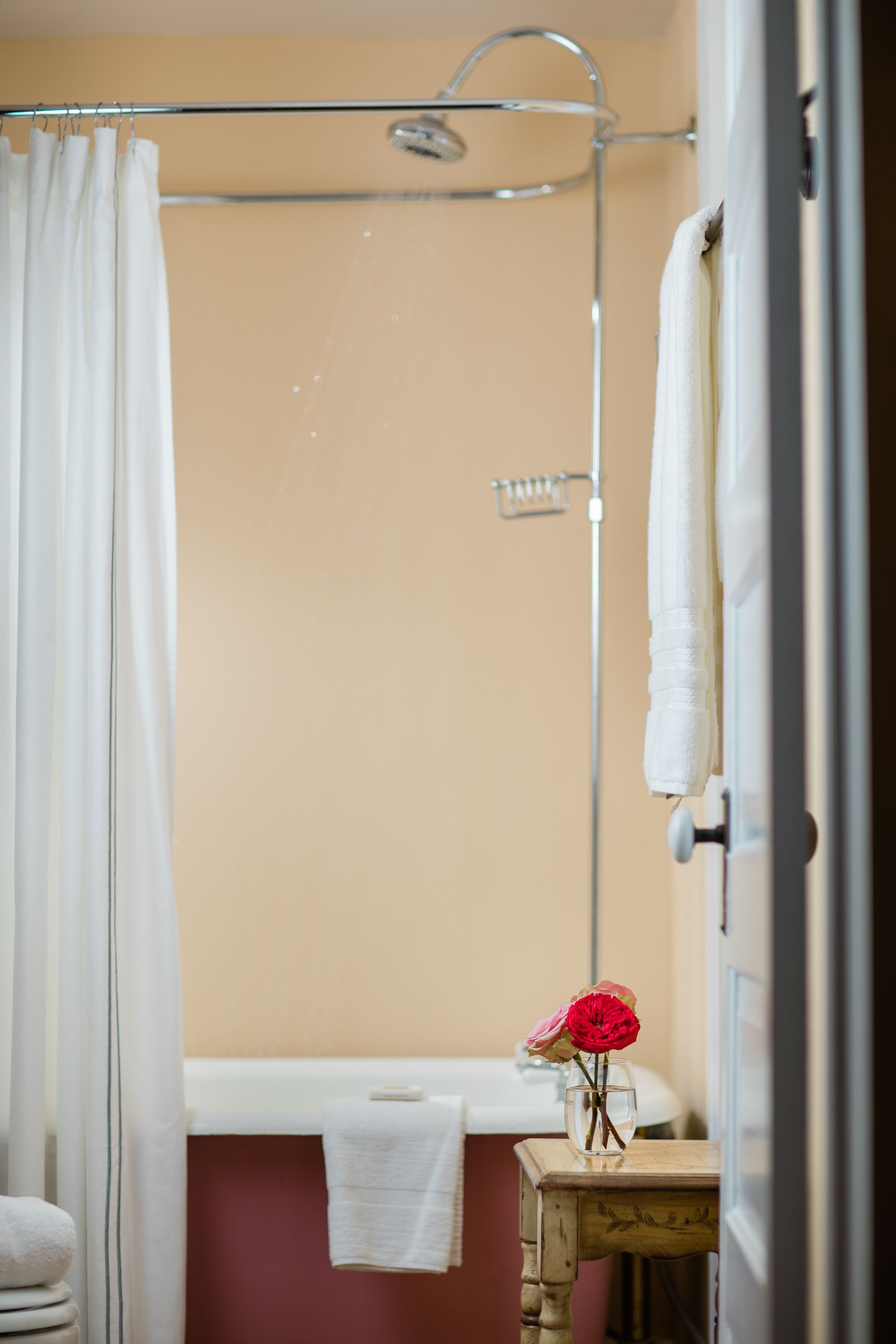 A bathroom with a shower, a bathtub, and a small table with a vase of flowers.