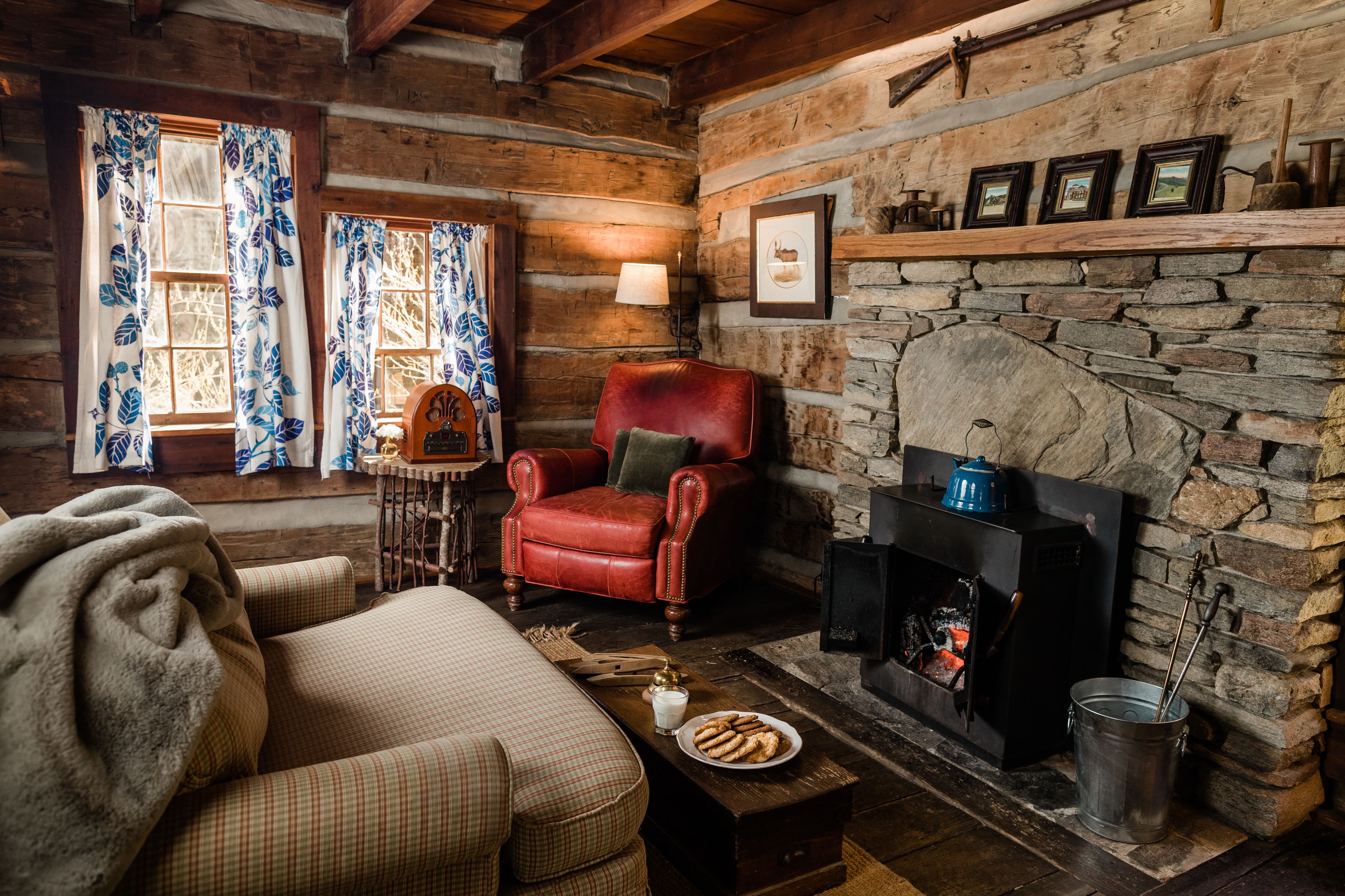 Interior acogedor de una cabaña de troncos con chimenea, un sillón de cuero rojo y un sofá a cuadros.
