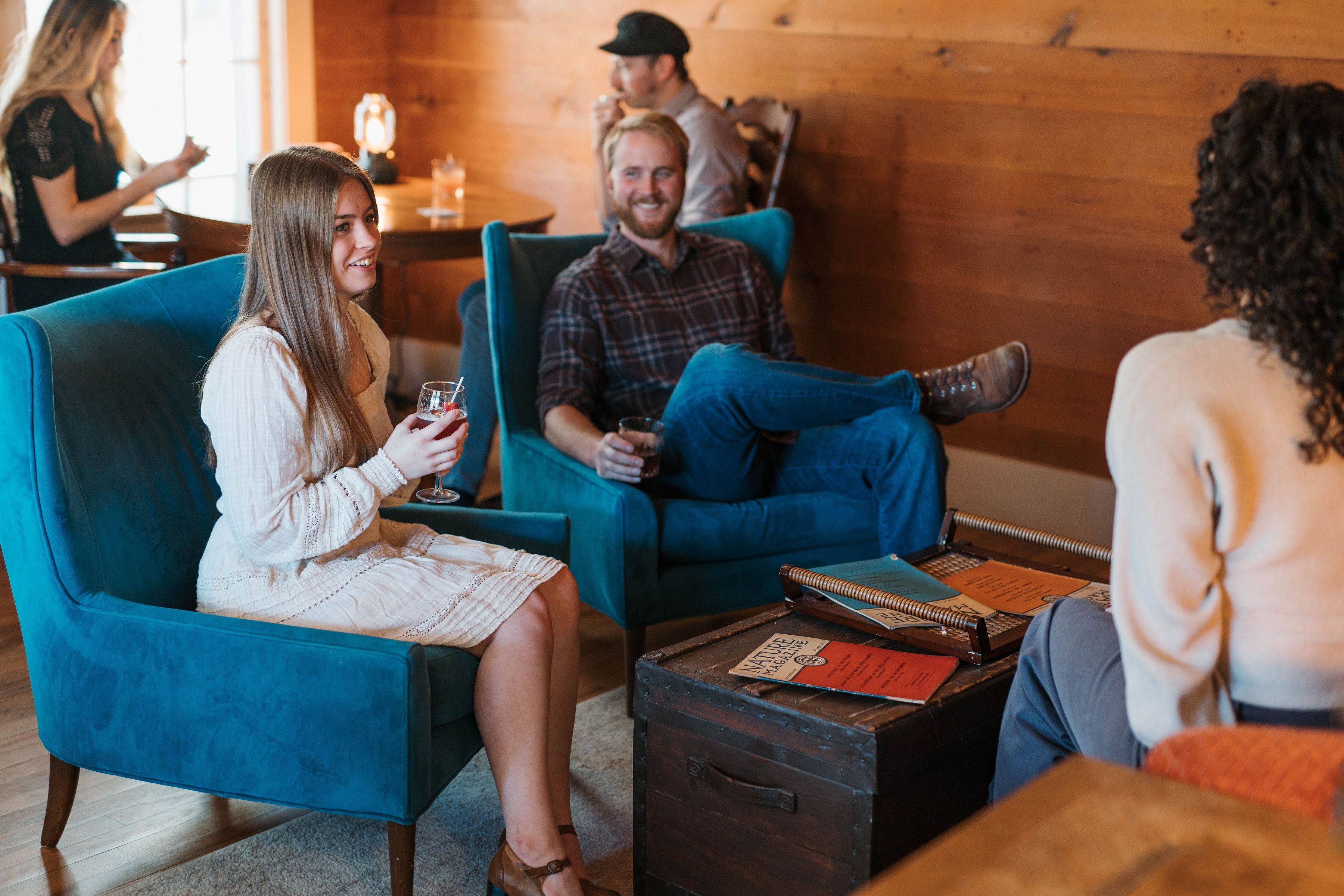 A cozy indoor setting with teal armchairs, wooden tables, and a rustic wooden wall.