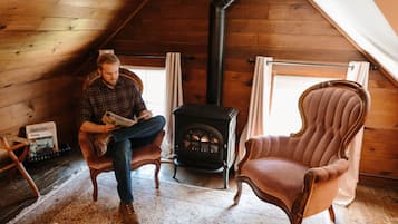 Una habitación acogedora con techo de madera, chimenea, sillón de cuero y una persona leyendo un libro.
