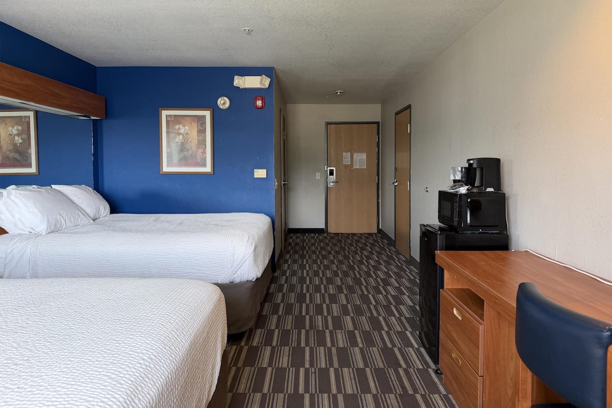 A hotel room with two beds, a desk with a coffee maker, and a door leading to another room.