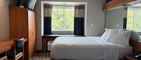 A hotel room with a bed, a desk, a chair, a TV, and a window with curtains.
