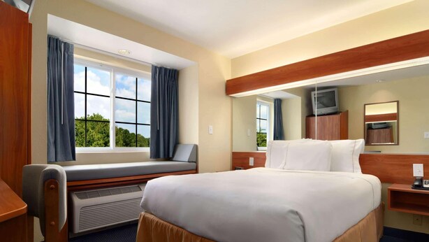 A hotel room with a large bed, a desk, a chair, a window with curtains, a television on a cabinet, and a mirror on the wall. - SureStay by Best Western Huntsville East (Huntsville)