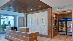 Zona de recepción con mostrador de madera, pared con diseño y vitrina refrigerada con bebidas.