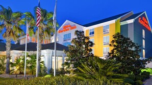 Un hotel Hilton Garden Inn con diseño moderno, que destaca una bandera estadounidense y palmeras en primer plano.