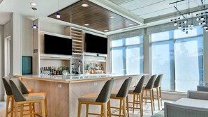 Zona de bar moderna con un televisor grande, taburetes y una alacena repleta de licores.