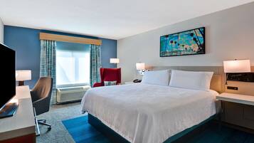 A hotel room with a large bed, a desk with a computer, a red chair, and a painting on the wall.