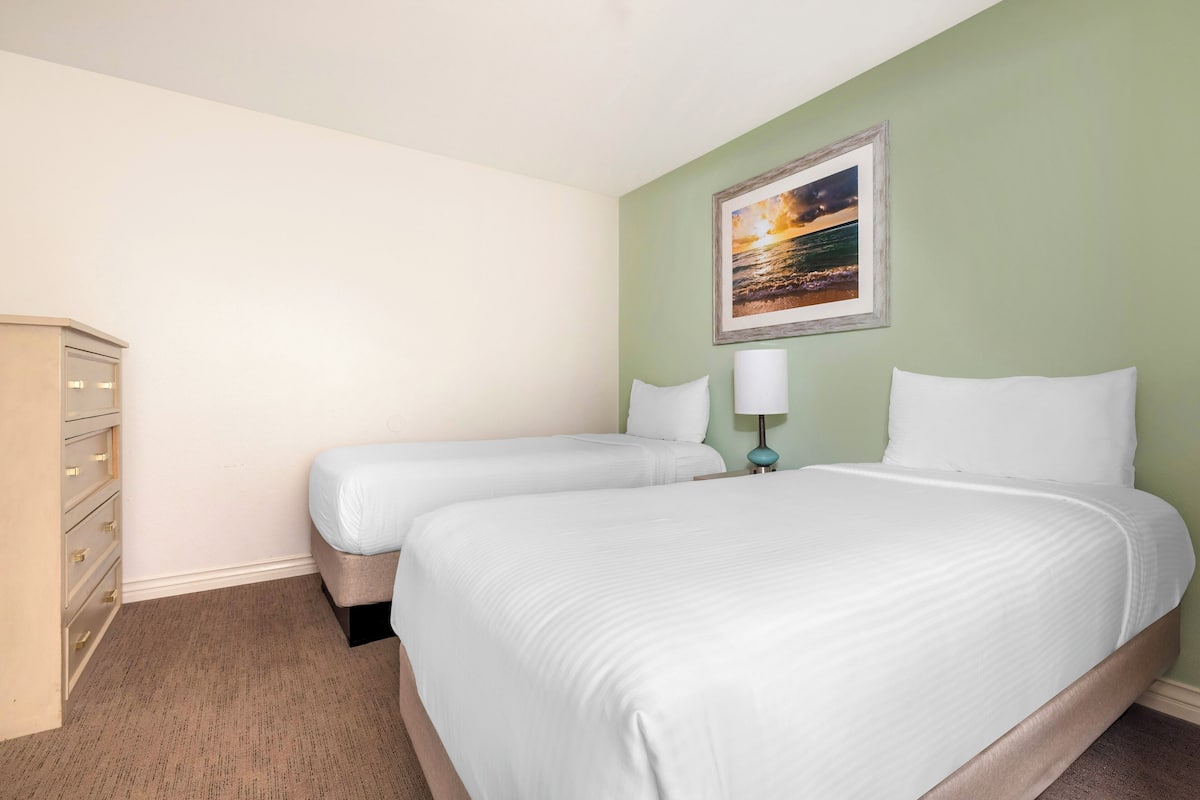 Ein Hotelzimmer mit zwei Einzelbetten, einem Schminktisch, einem Nachttisch mit Lampe und einem gerahmten Bild an der Wand.