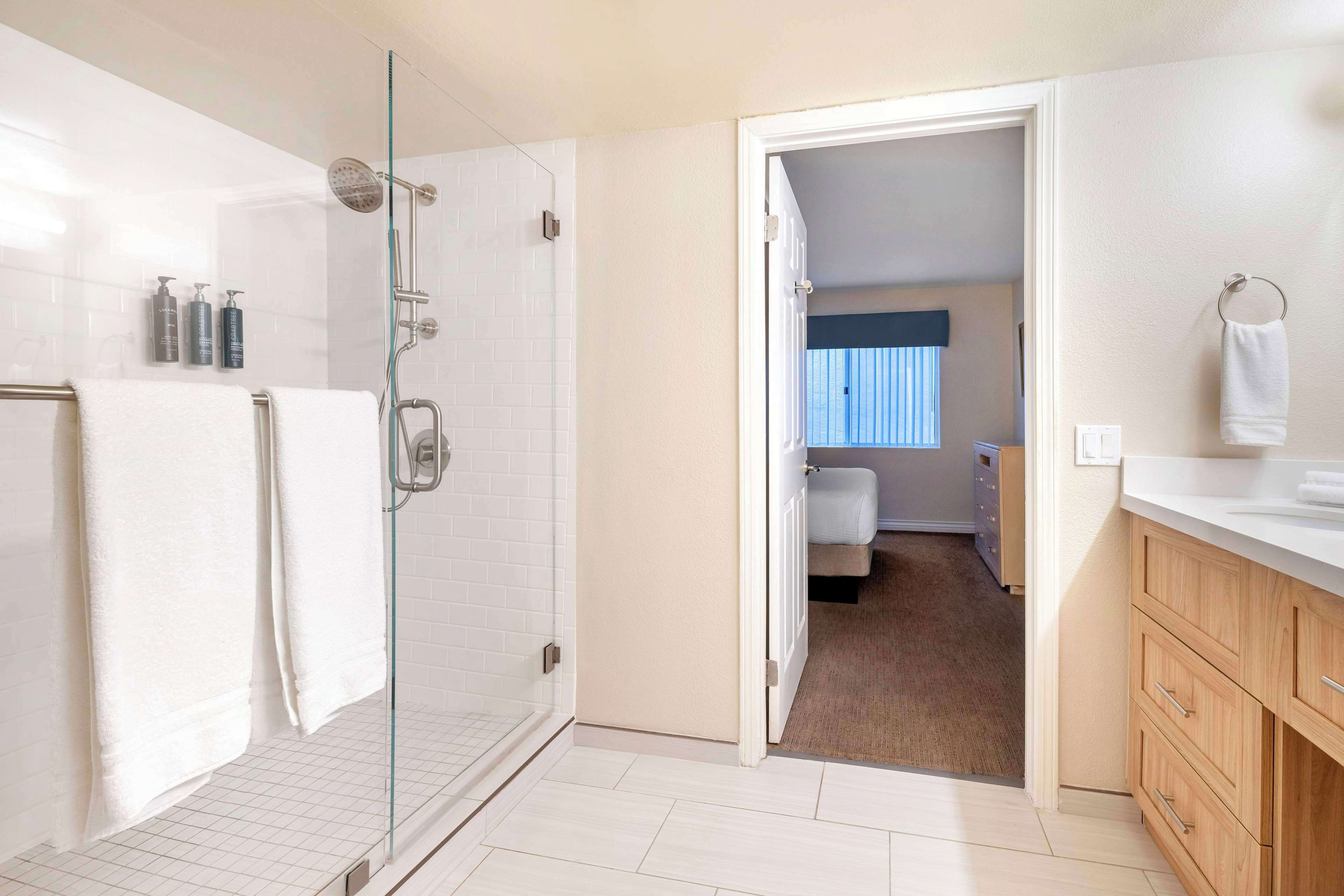A modern bathroom with a glass shower enclosure, white tiles, and a wooden vanity.
