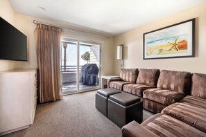 A hotel room with a sofa, ottoman, flat-screen TV, sliding glass door, and a painting of a beach scene. - Hilton Vacation Club Riviera Beach & Shores (Dana Point)