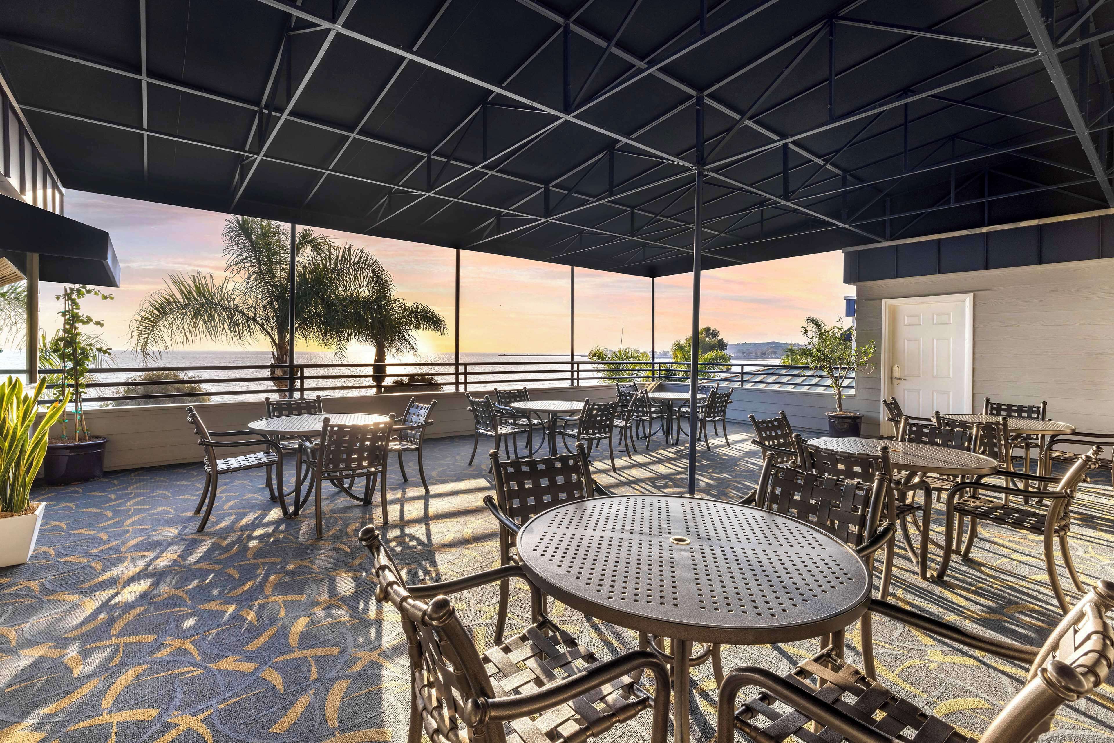 A covered outdoor seating area with tables and chairs, overlooking a body of water.