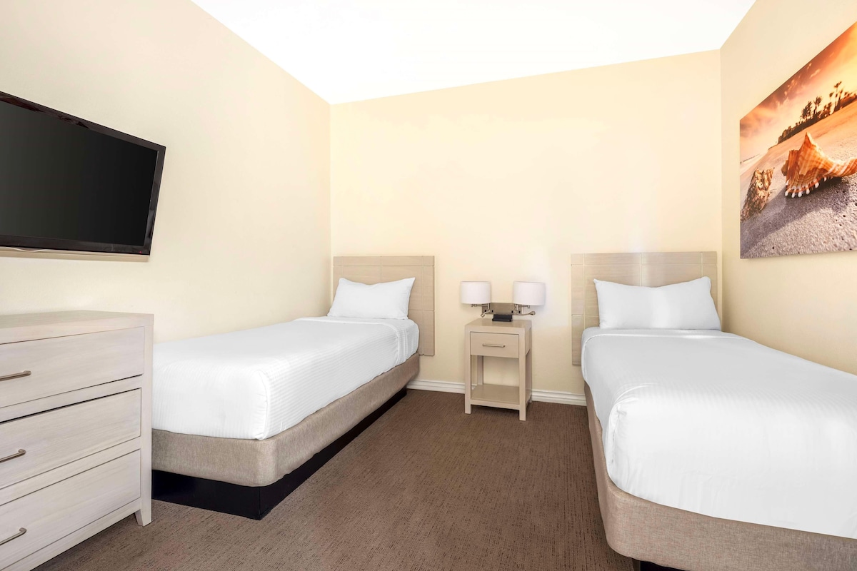 A hotel room with two beds, a flat-screen TV, a dresser, and a painting on the wall.