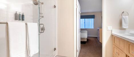 A modern bathroom with a glass shower enclosure, white tiles, and a wooden vanity with a towel rack.