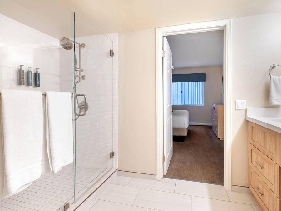 A modern bathroom with a glass shower enclosure, white tiles, and a wooden vanity with a towel rack.