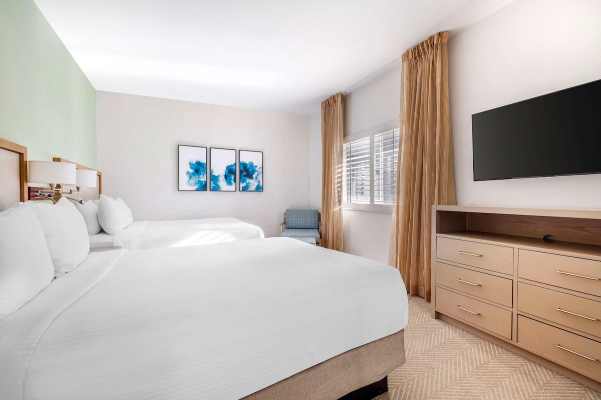 A hotel room with two beds, a flat-screen TV, a desk, and a chair.