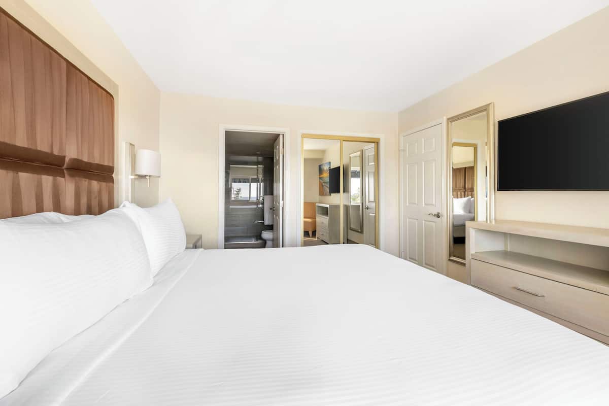 Ein Hotelzimmer mit einem großen Bett, einem Kleiderschrank, einem Fernseher und einem durch eine offene Tür einsehbaren Badezimmer.