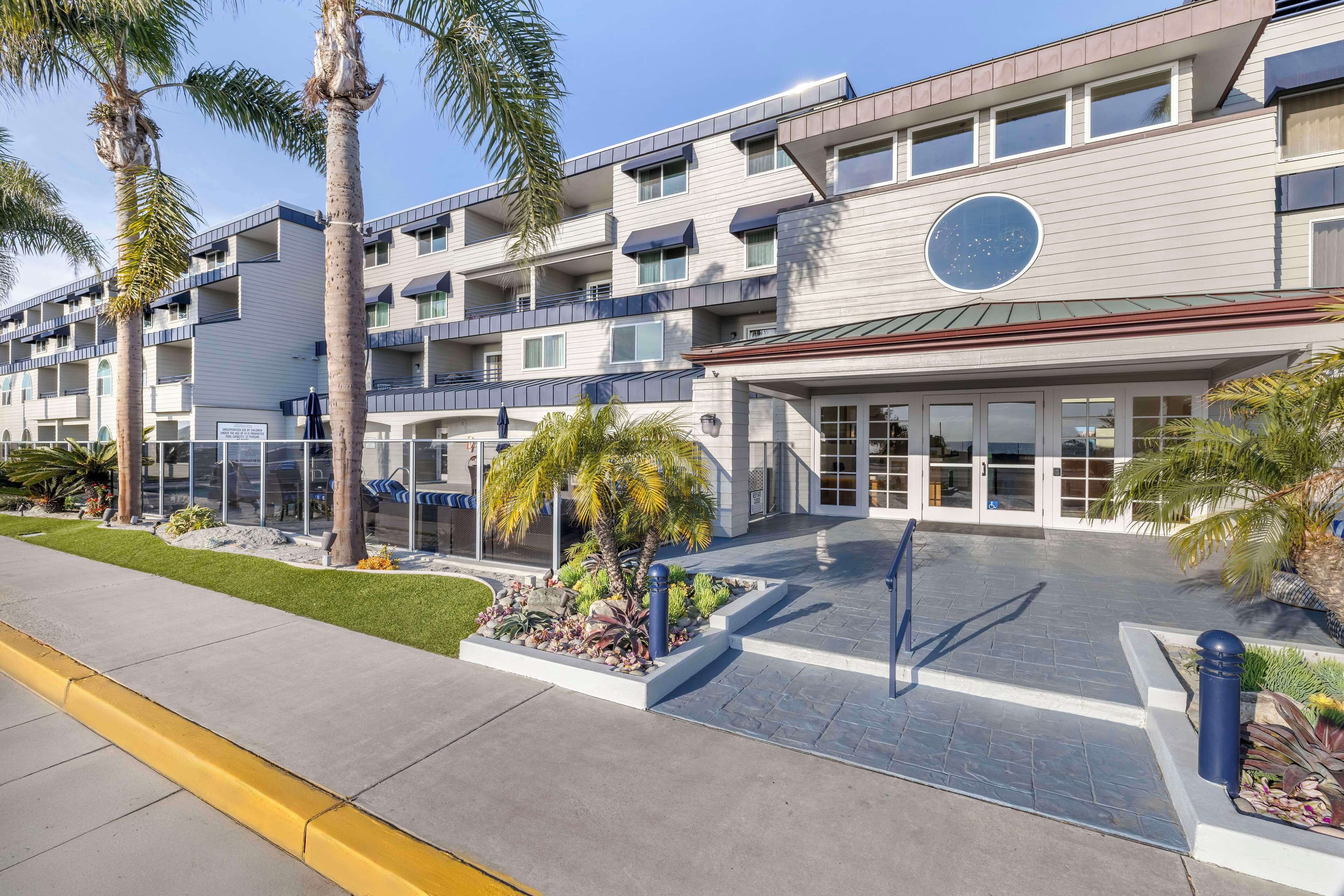 Un hotel moderno de varios pisos con entrada central, balcones y un patio ajardinado.