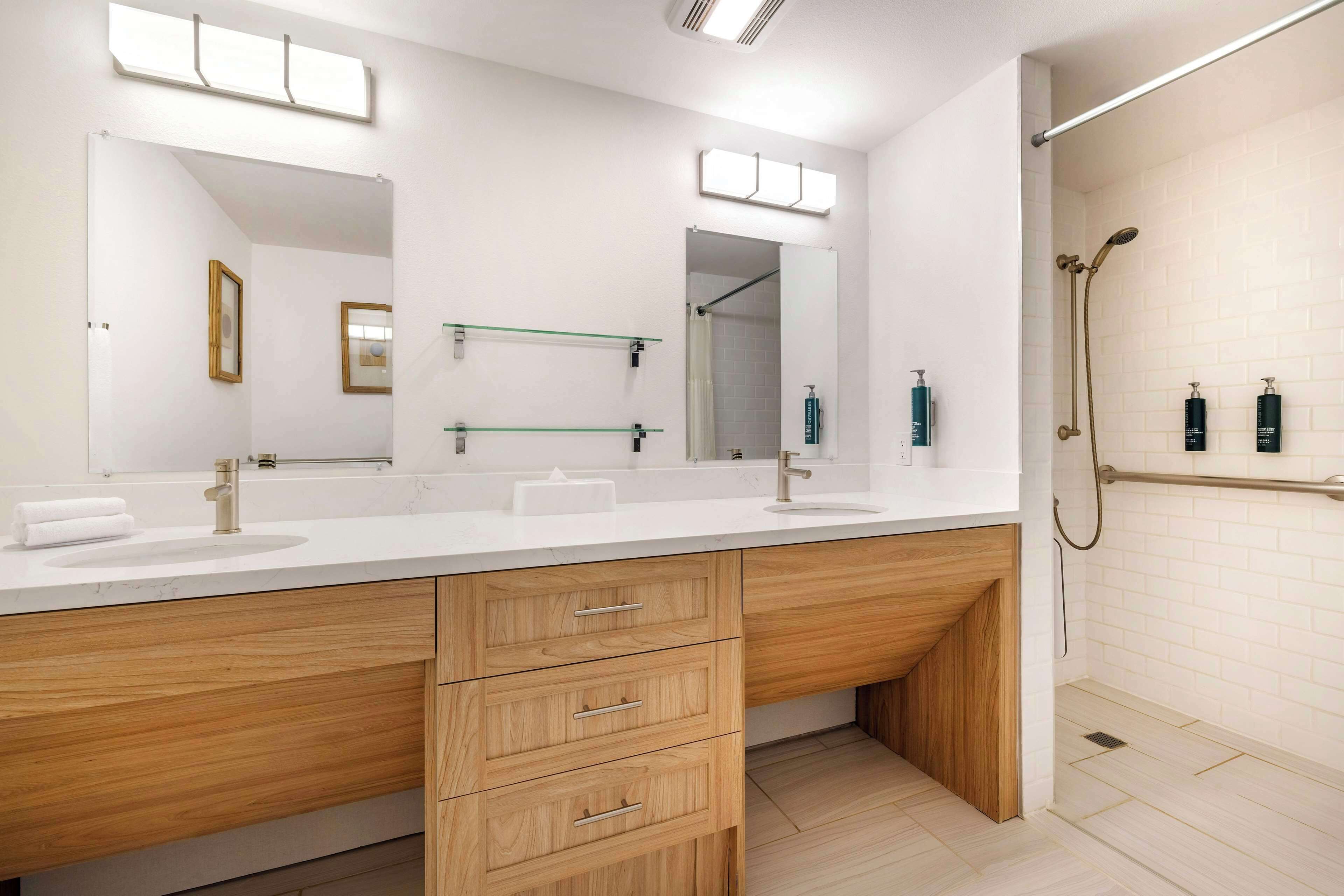 Une salle de bain moderne avec deux vasques, des meubles en bois, un grand miroir et un espace douche.