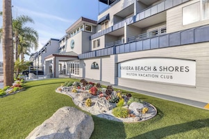 Exterior moderno de un hotel con un jardín ajardinado y un cartel que dice "Riviera Beach & Shores Hilton Vacation Club".