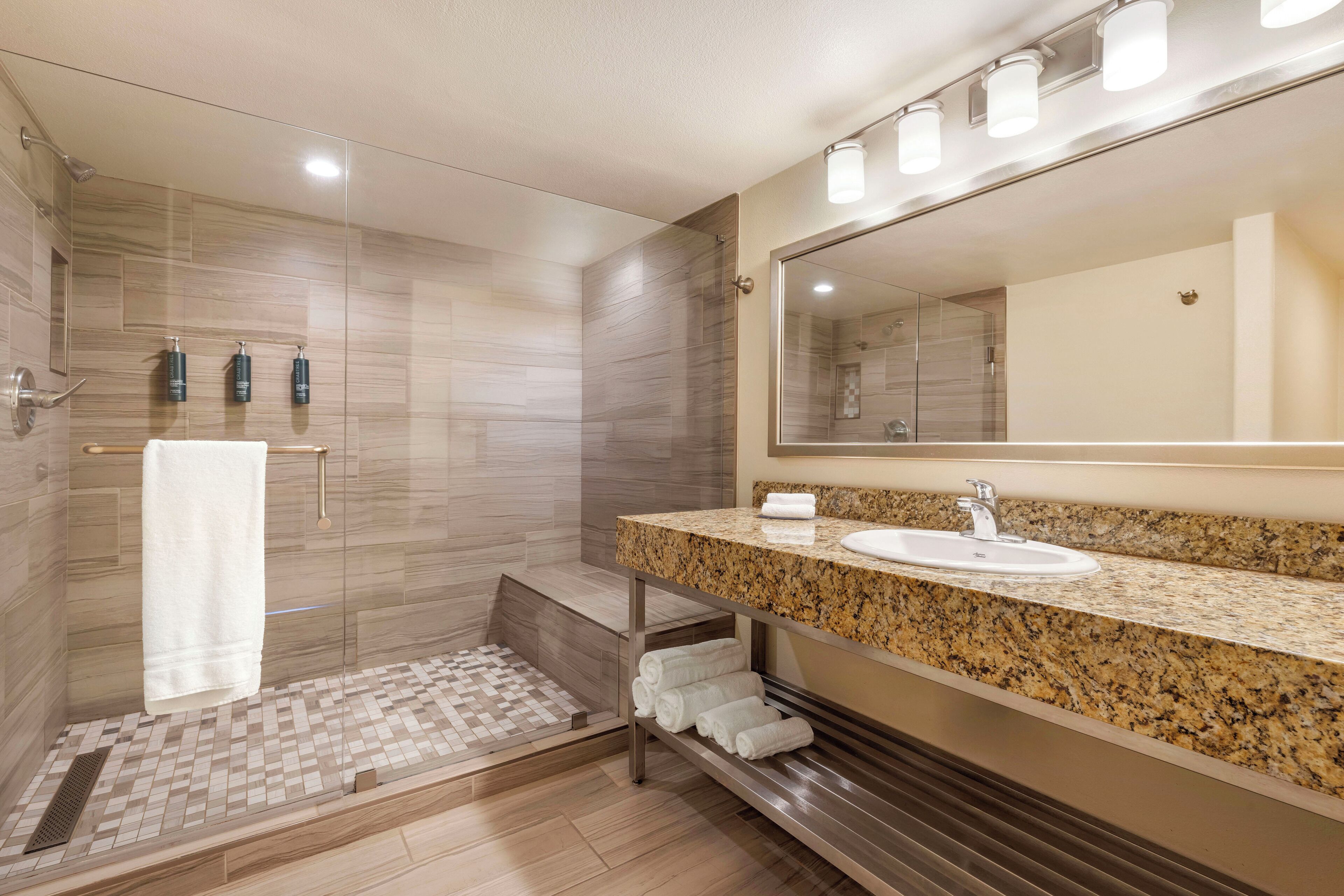 A modern bathroom with a glass-enclosed shower, a granite countertop sink, and a large mirror.