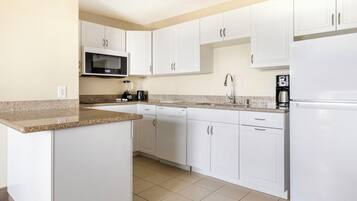 A modern kitchen with white cabinets, a granite countertop, a built-in microwave, a coffee maker, and a dishwasher.