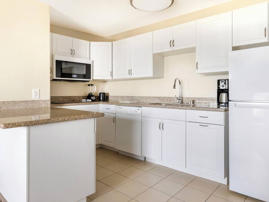 A modern kitchen with white cabinets, a granite countertop, a built-in microwave, a coffee maker, and a dishwasher.