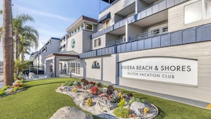 Exterior moderno de hotel con jardín ajardinado y un letrero que dice "Riviera Beach & Shores Hilton Vacation Club".