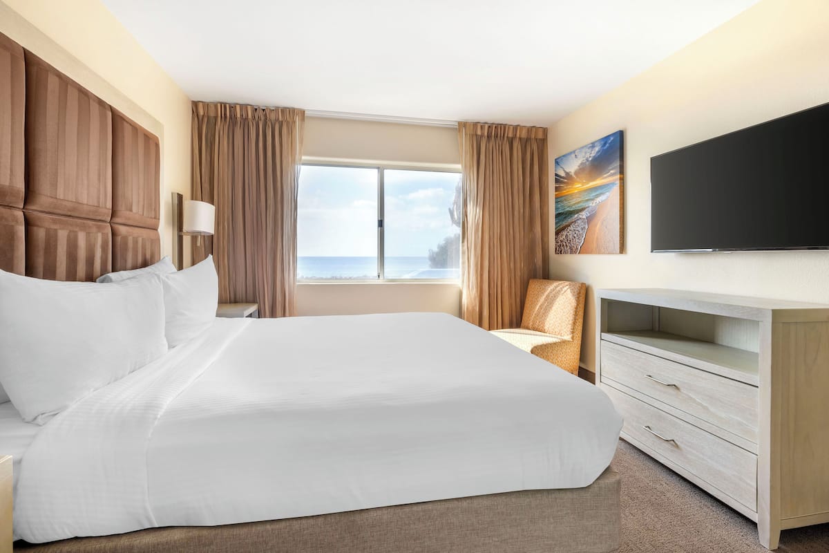 Ein Hotelzimmer mit einem großen Bett, einem Flachbildfernseher, einem Schreibtisch und Blick auf den Ozean.