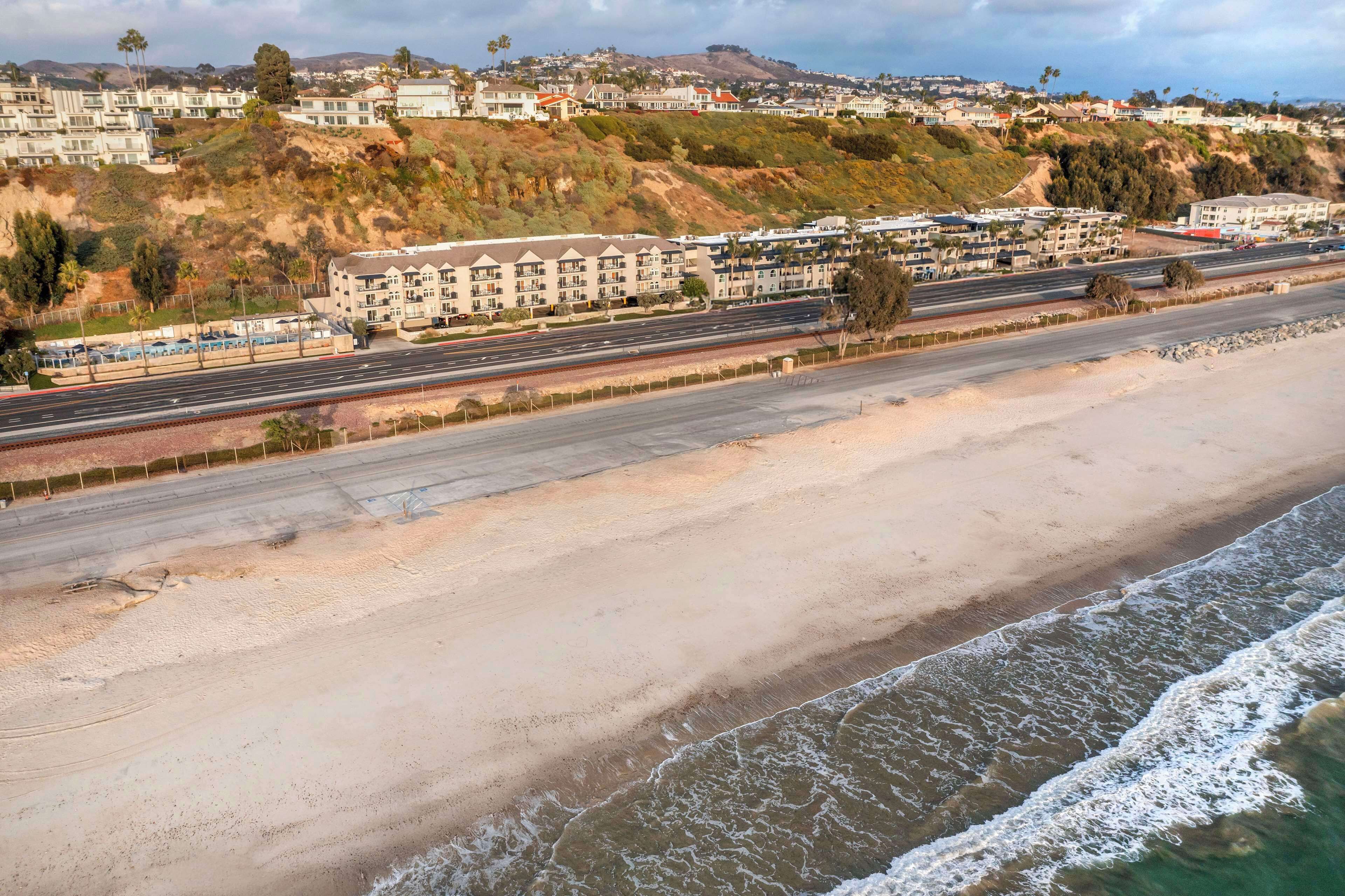 Une route côtière bordée d’une plage, avec des immeubles résidentiels en arrière-plan.