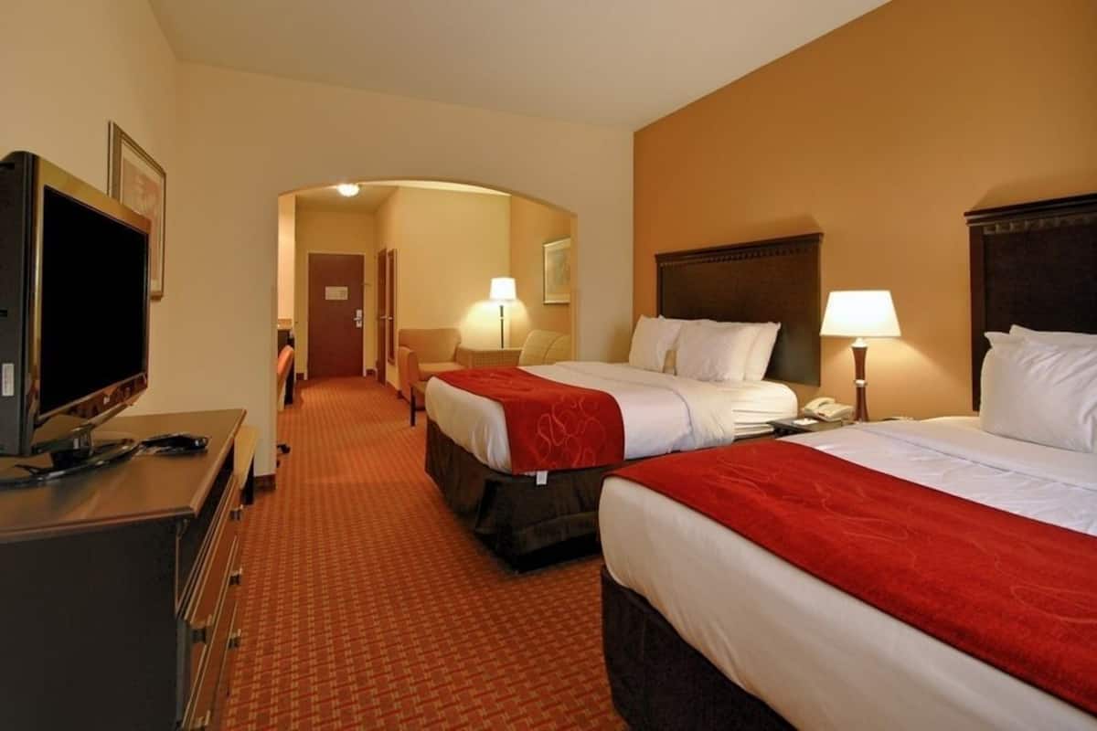 A hotel room with two beds, a television, a desk, and a hallway leading to another room.