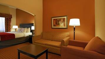 A hotel room with a bed, two chairs, a table, a lamp, and a painting on the wall.