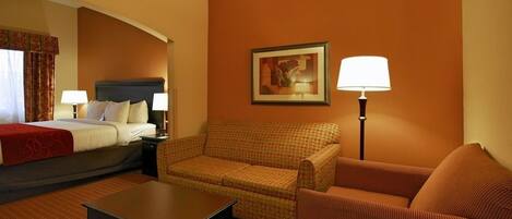 A hotel room with a bed, two chairs, a table, a lamp, and a painting on the wall.