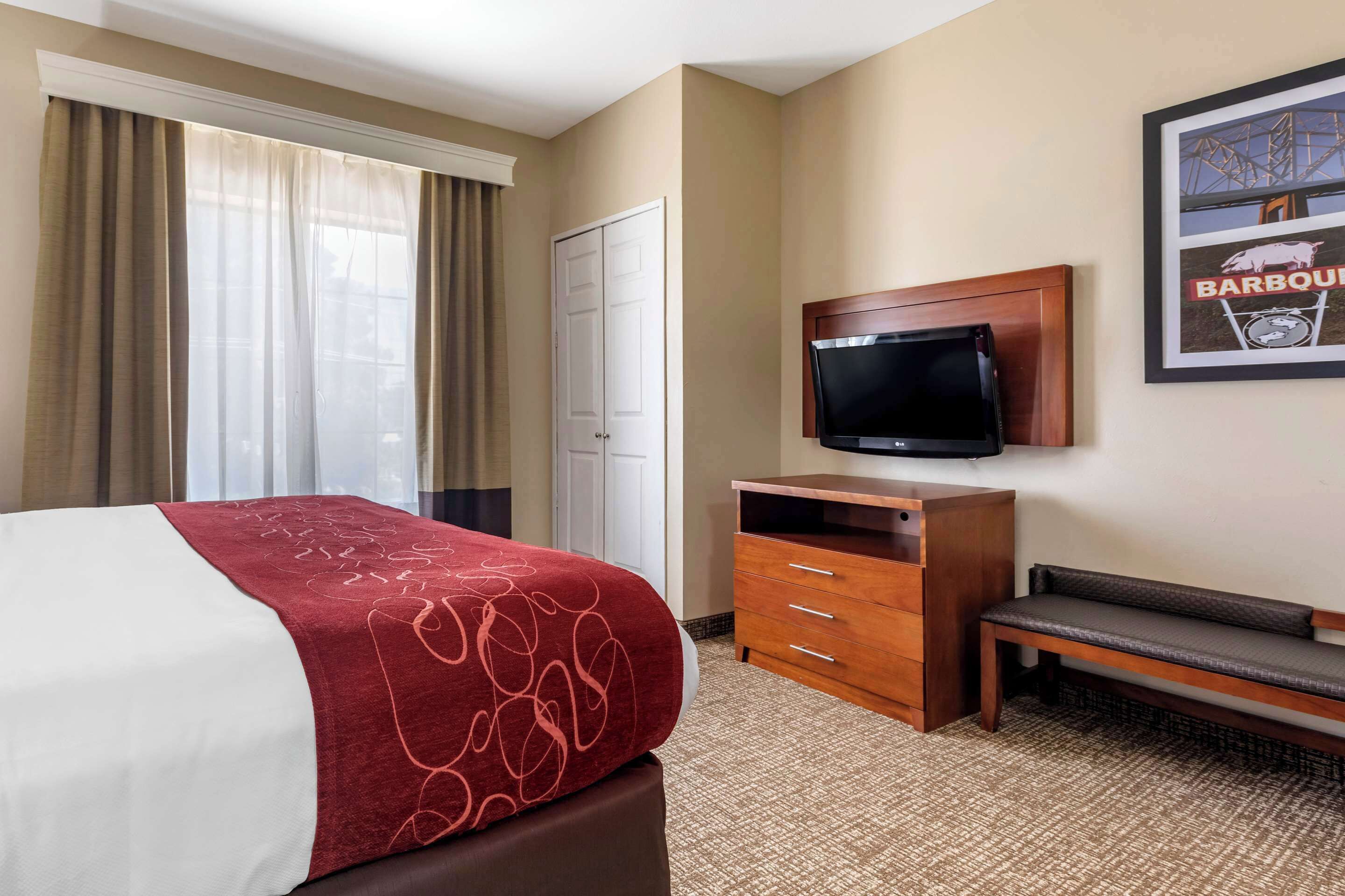 Una habitación de hotel con una cama, televisión, un banco de madera y una puerta.