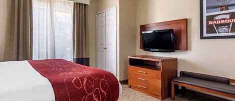 Una habitación de hotel con una cama, televisión, un banco de madera y una puerta.