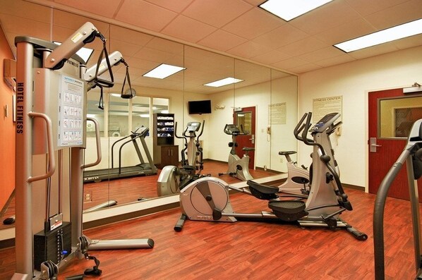A fitness center with exercise equipment, a mirrored wall, and a television.
