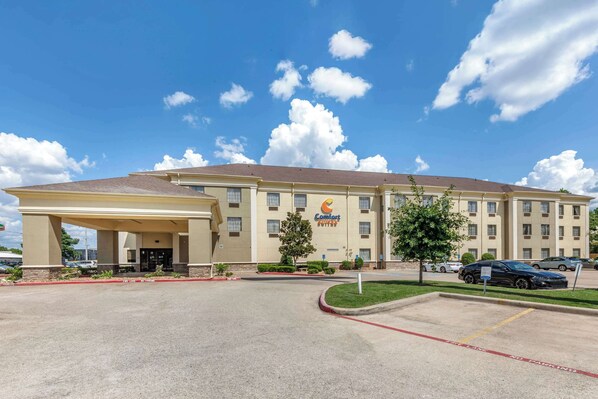 Un hotel Comfort Inn con entrada cubierta, estacionamiento y un cielo azul despejado con nubes.