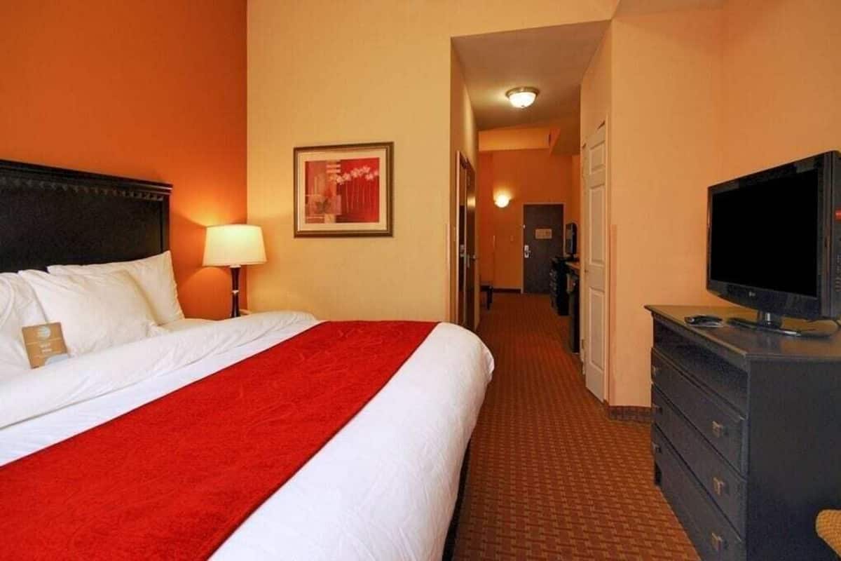 A hotel room with a bed, a television, a dresser, and a hallway leading to a door.