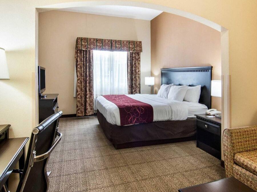 Une chambre d’hôtel avec un lit, un bureau, une chaise, une télévision et une fenêtre avec des rideaux.