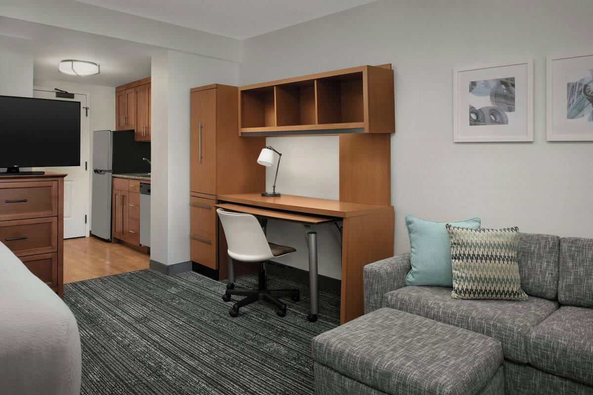A compact living space with a kitchenette, a desk with a chair, a sofa, and a television.