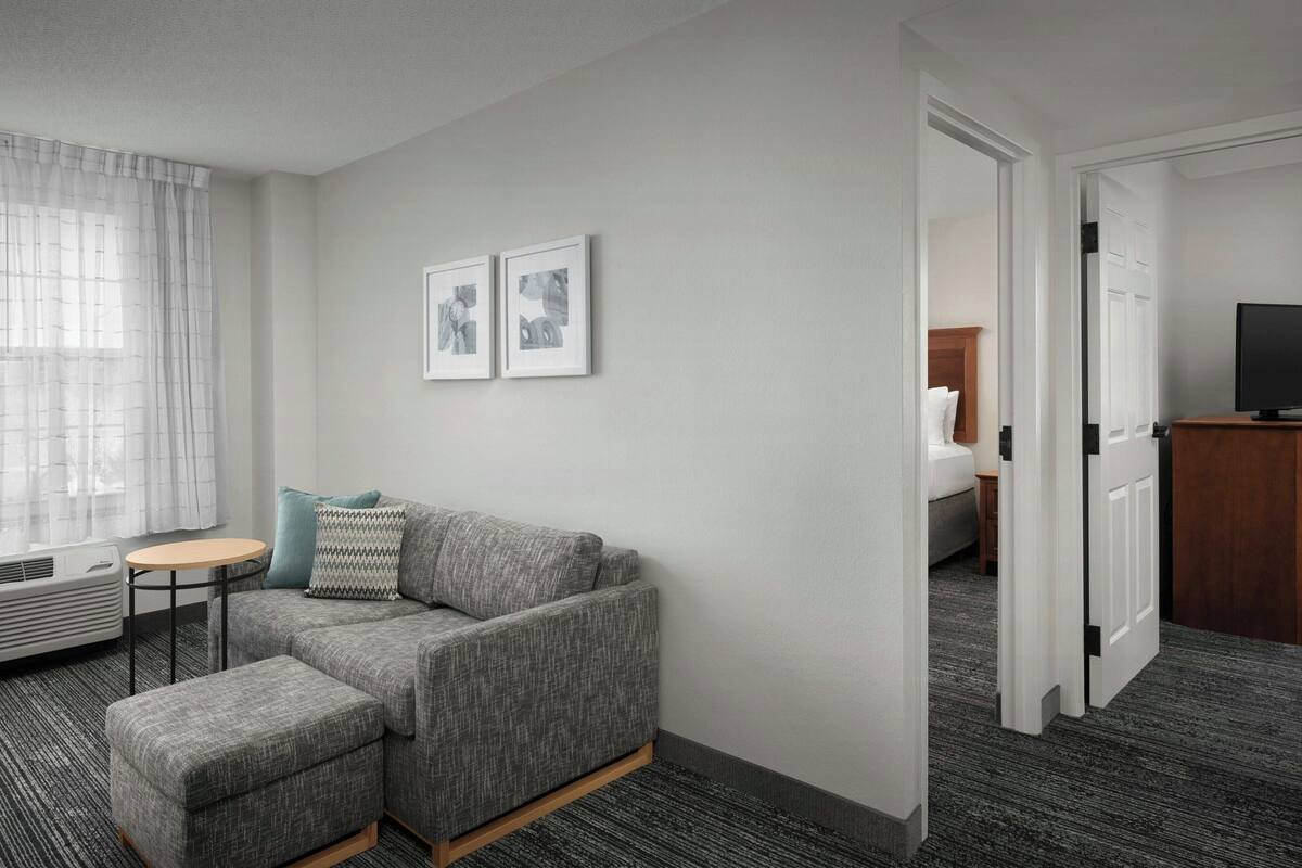 A modern hotel room with a grey sofa, a small round table, and a flat-screen TV.