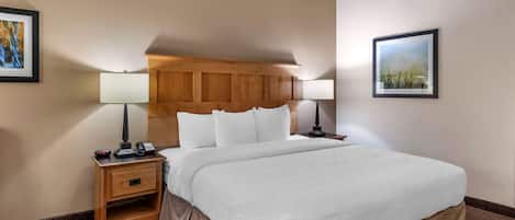 A hotel room with a large bed, wooden headboard, two bedside tables with lamps, and framed pictures on the walls.