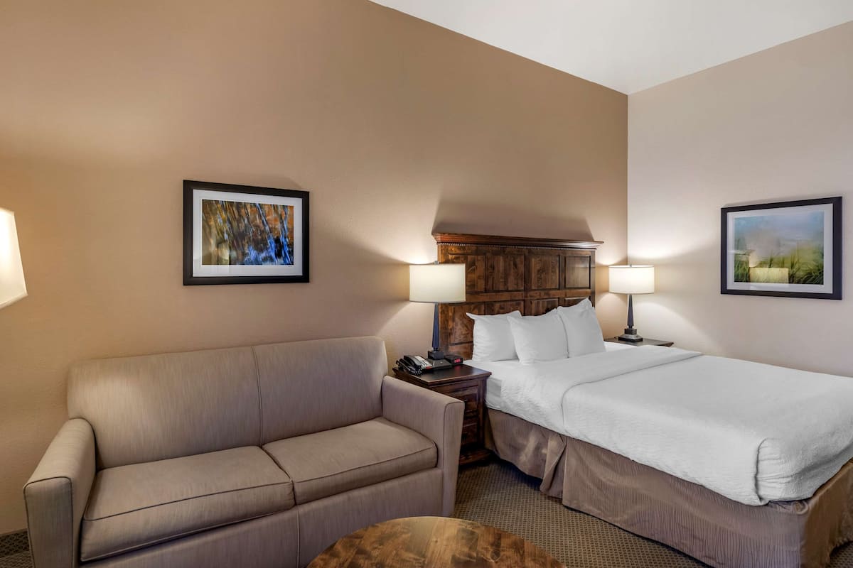 A hotel room with a bed, a sofa, a nightstand, and two wall-mounted lamps.