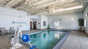 Une piscine intérieure avec un mur en verre transparent, une chaise bleue et un dispositif d’élévation pour faciliter l’accès à la piscine.