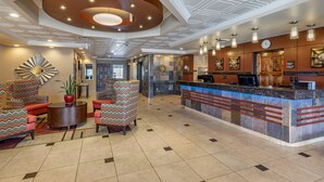 Un hall d’hôtel comprenant un comptoir d’accueil, un espace salon avec des fauteuils à motifs et un plafond décoratif.