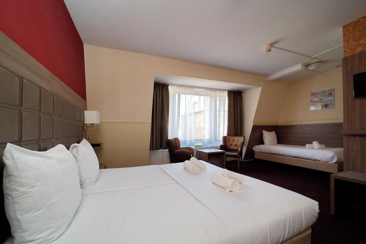 Une chambre d’hôtel avec un grand lit, un lit plus petit, un bureau, une chaise et un téléviseur.